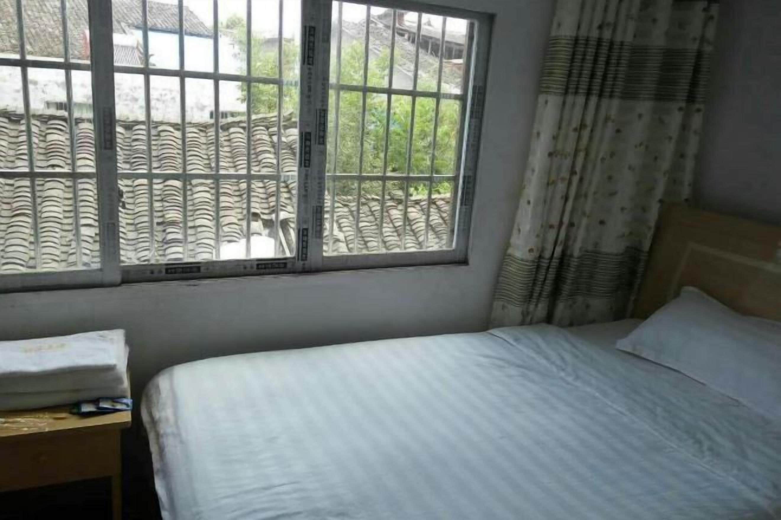 A bedroom with a bed, a window with bars, and a curtain.