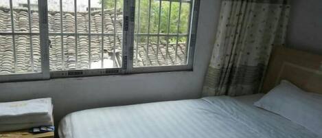 A bedroom with a bed, a window with bars, and a curtain.