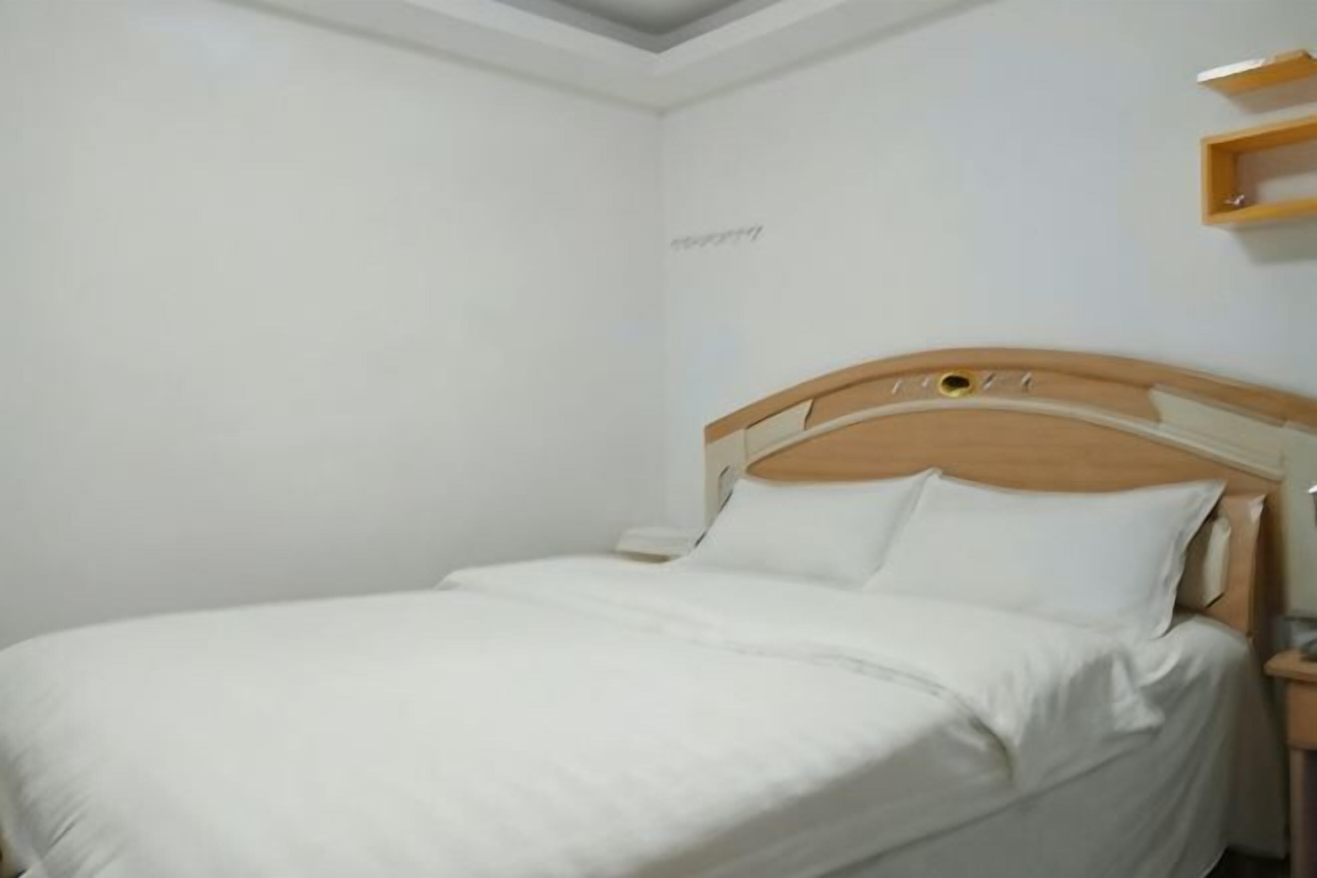A single bed with a wooden headboard, a bedside table, and a wall-mounted shelf.