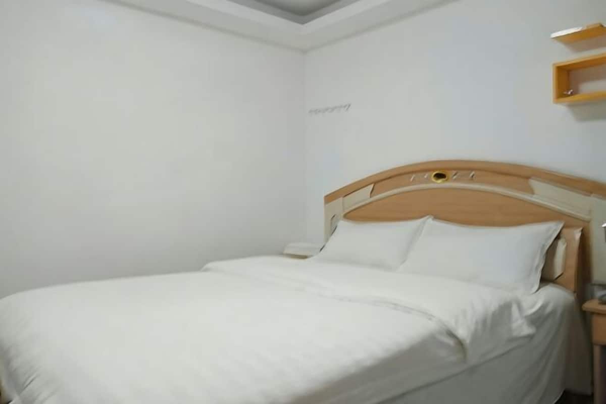 Ein Einzelbett mit Holz-Kopfteil, einem Nachttisch und einem an der Wand befestigten Regal.