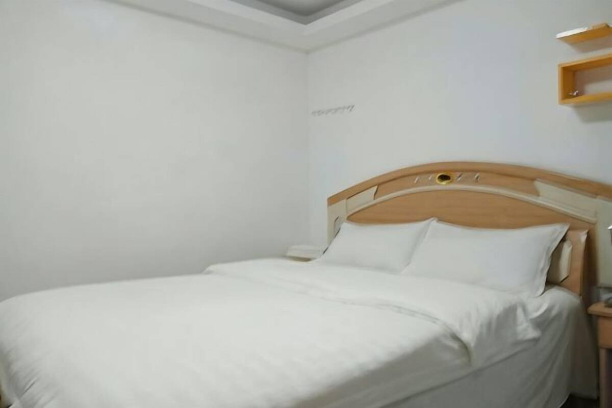 A single bed with a wooden headboard, a bedside table, and a wall-mounted shelf.