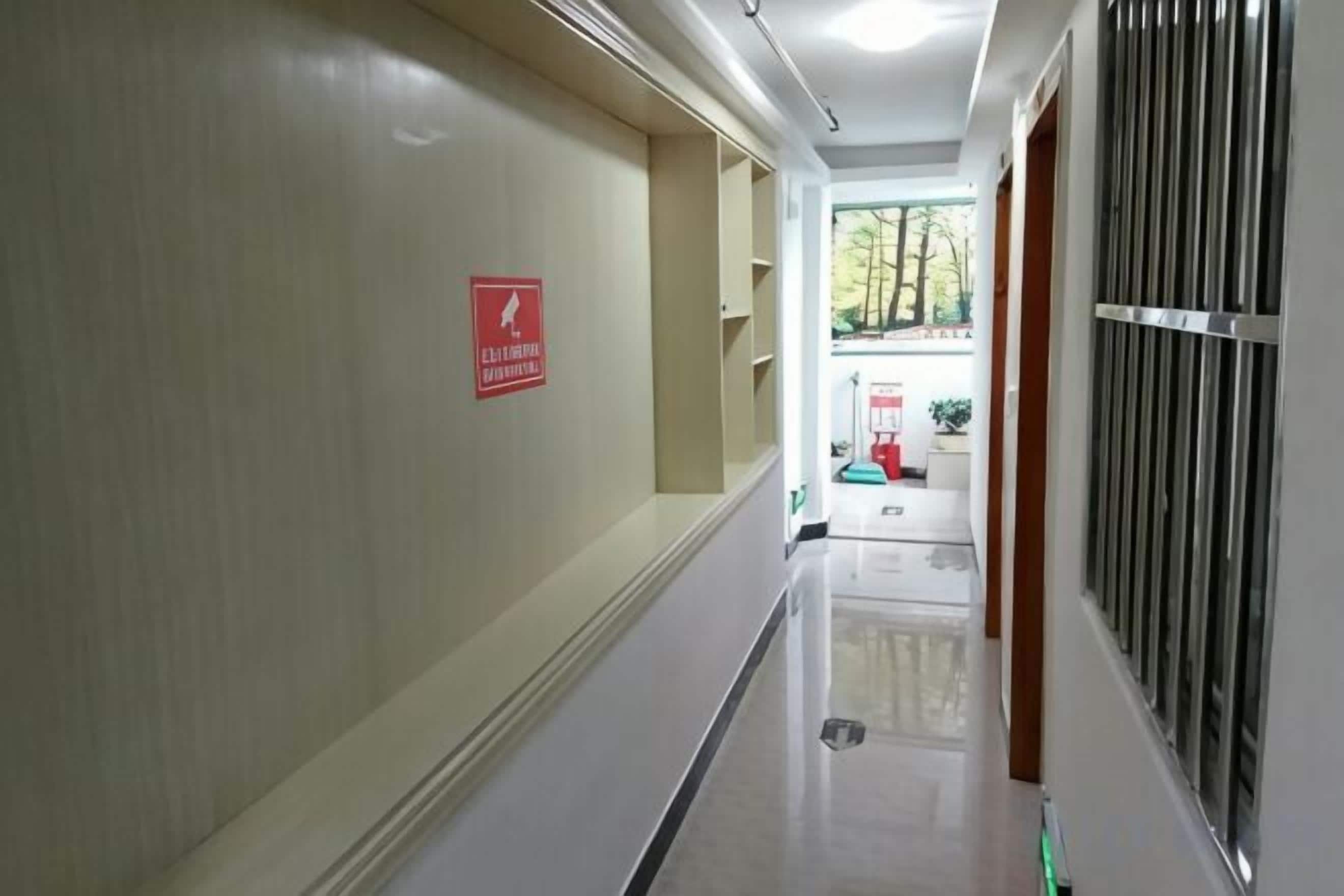 A hallway with a fire exit sign, a trash bin, and a door leading to an outdoor area.