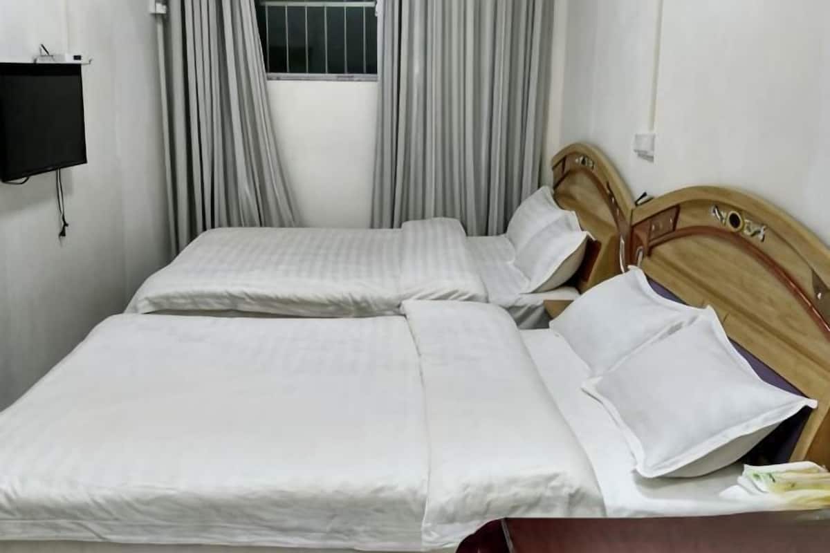 Ein Doppelbett mit weißer Bettwäsche und einem Holzkopfende, ein Nachttisch und ein Fenster mit Vorhängen.