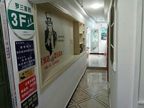 A hotel corridor with a reception desk, a poster with a figure, and a tiled floor. - Fenggang Luosan Inn (Fenggang)