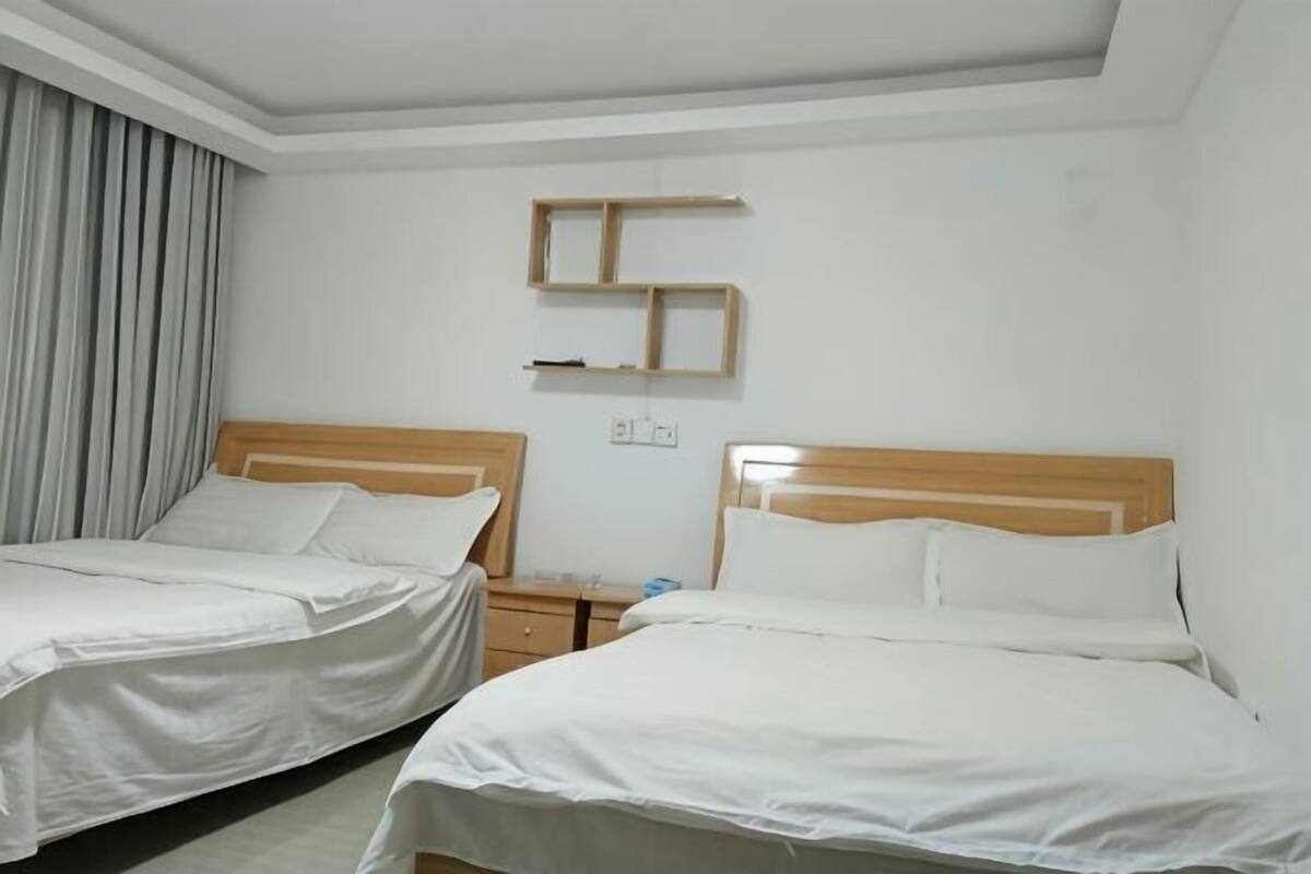 Ein Hotelzimmer mit zwei Betten, einem Nachttisch, einem Wandregal und einem Vorhang.