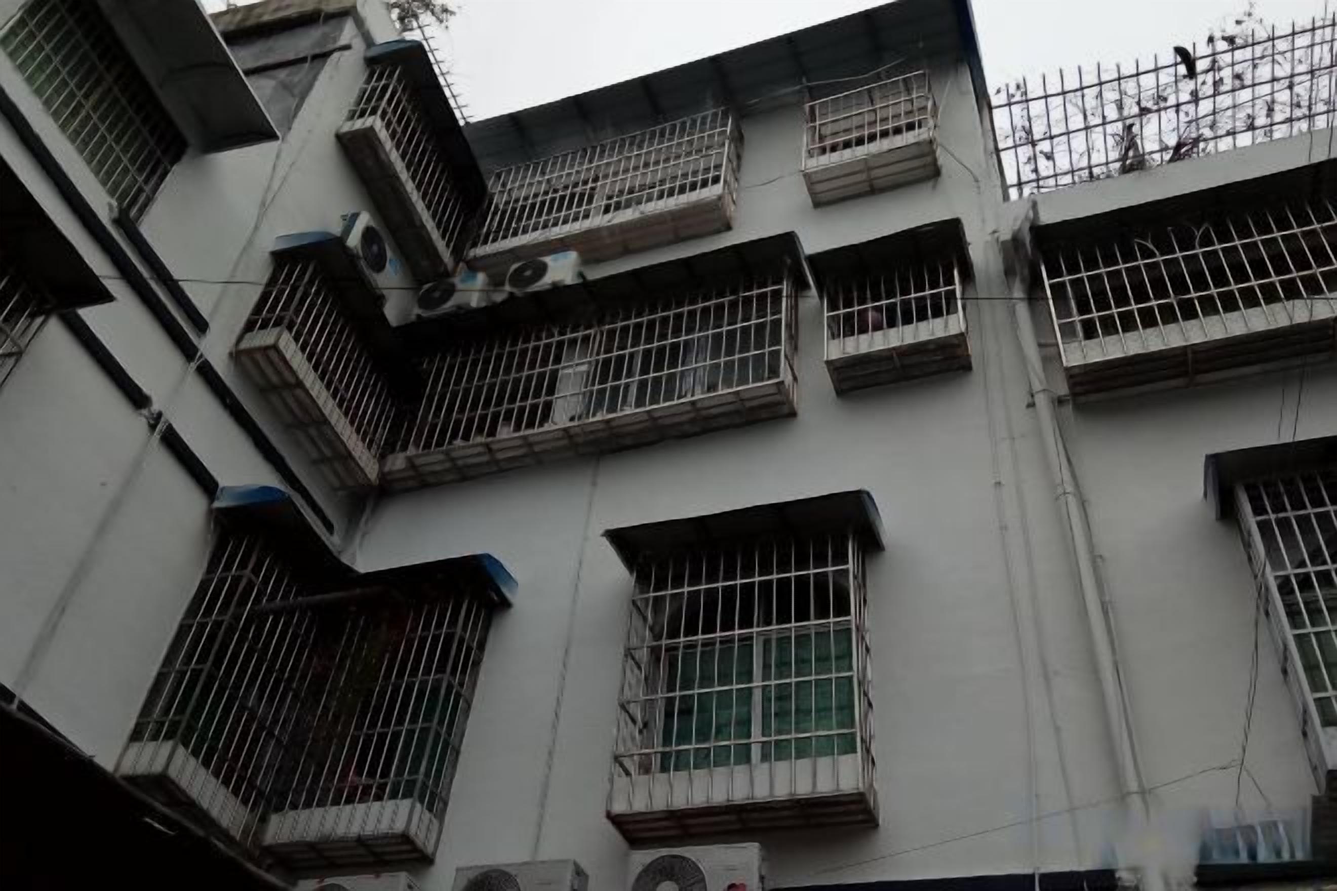 Un edificio de varios pisos con ventanas protegidas por barrotes y balcones, que presenta un patrón de cuadrícula en sus ventanas y unidades de aire acondicionado.