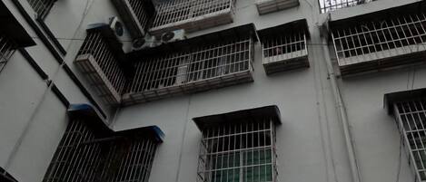 Un immeuble à plusieurs étages, doté de fenêtres grillagées et de balcons, dont la façade présente un motif géométrique régulier composé de fenêtres et de climatiseurs.