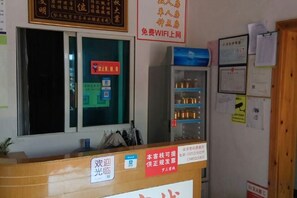Un mostrador de recepción con ventana, un refrigerador y varios carteles y avisos en la pared.