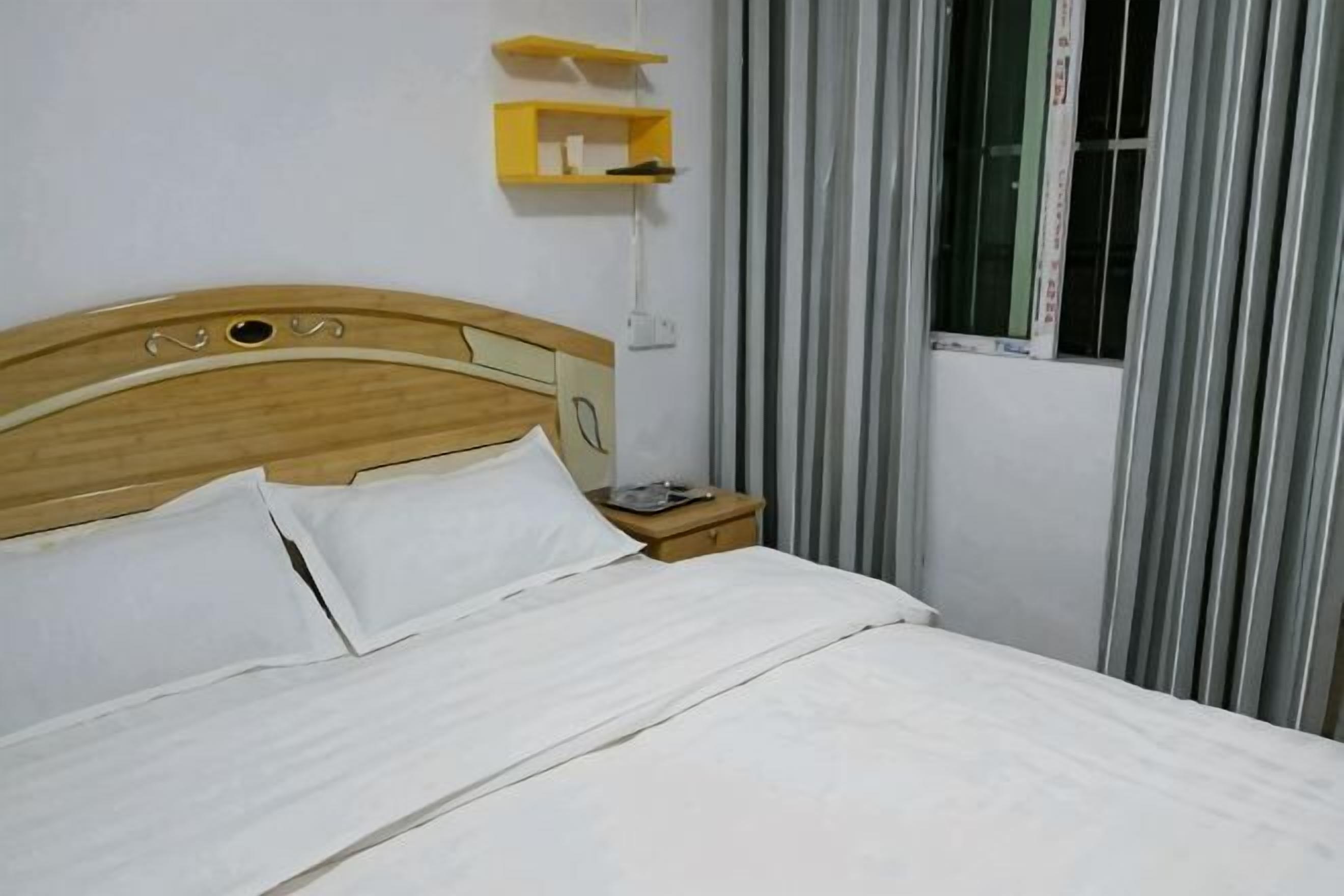 A bed with white linens, a wooden headboard, a bedside table with a lamp, and a window with curtains.
