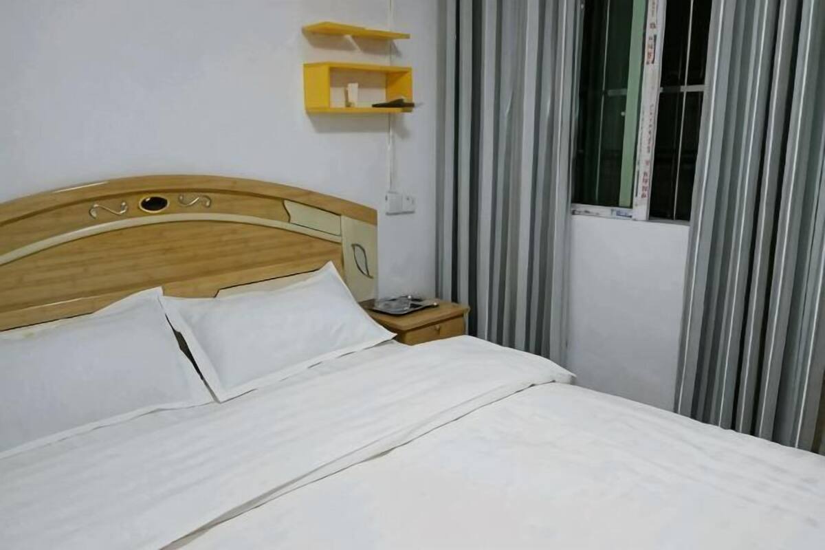 Ein Bett mit weißer Bettwäsche, ein Holz-Kopfende, ein Nachttisch mit Lampe und ein Fenster mit Vorhängen.