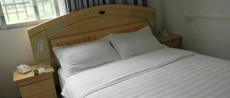 A single bed with a wooden headboard, a bedside table with a lamp, and a window with curtains.