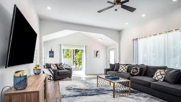 A modern living room with a large TV, two sofas, a coffee table, and a ceiling fan. - Castaway Villas: Perfect Group Getaway – Heated Pool & Hot Tub Access (New Buffalo)
