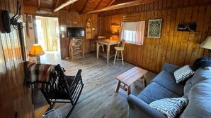 Interior acogedor de una cabaña de madera con sofá, una mesita, televisión y chimenea.