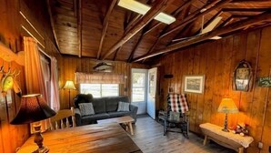 Un interior acogedor de cabaña con paredes y techo de madera, un sofá, una mesita y un banco.