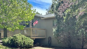 A residential house with a front deck, an American flag, and a well-maintained lawn.