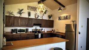 A kitchen with wooden cabinets, a stainless steel refrigerator, a bar counter with stools, and decorative plants.