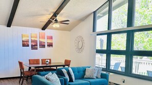 A spacious living room with a large blue sectional sofa, a glass coffee table, and a dining area with a wooden table and chairs.