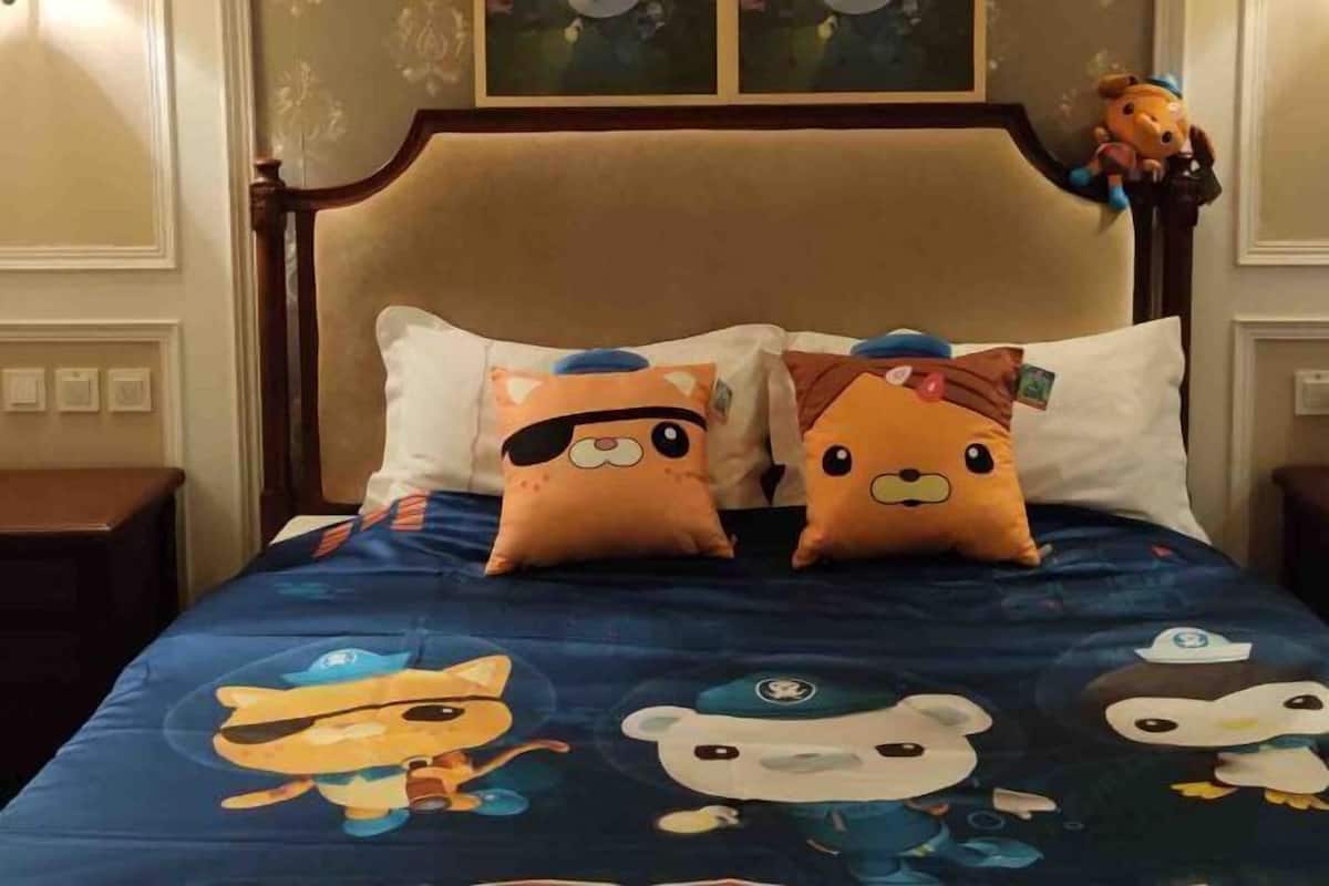 Ein Bett mit Kopfkissen mit Zeichentrickfiguren und einer blauen Bettdecke mit Tiermotiven.