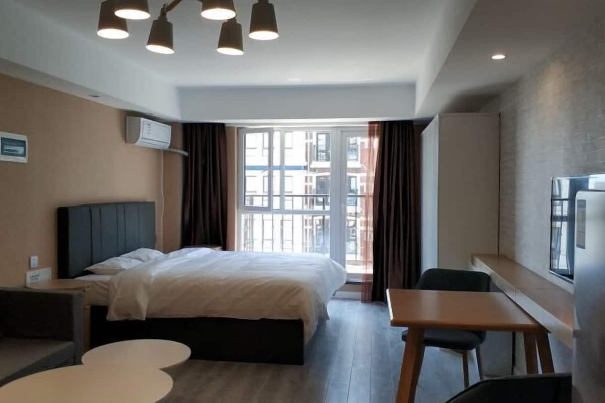 Ein Hotelzimmer mit Bett, Schreibtisch, Stuhl, rundem Tisch und Blick auf Gebäude durch das Fenster.