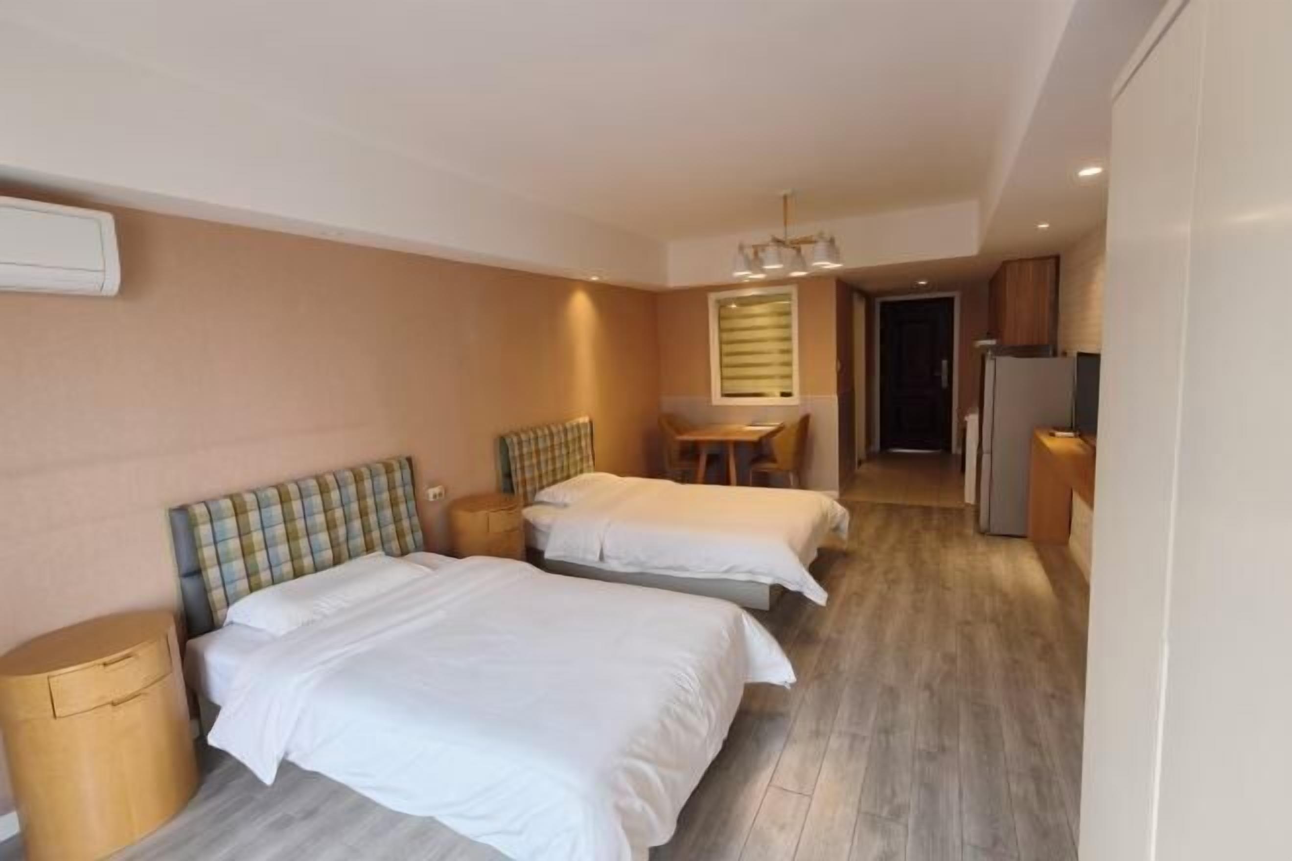 A hotel room with two beds, a desk, a chair, a refrigerator, and a trash bin.
