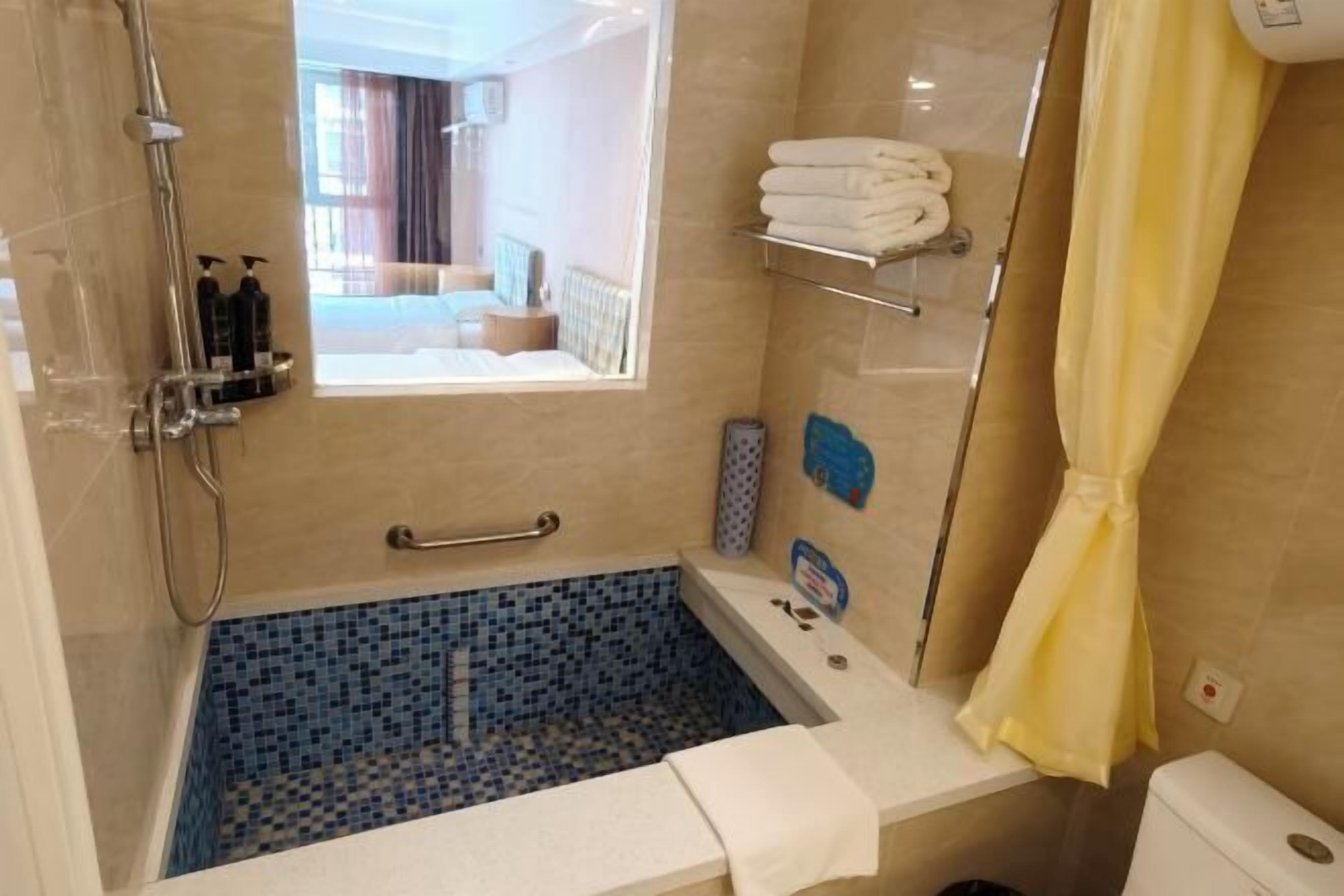 A bathroom with a blue-tiled bathtub, a shower, and a toilet.