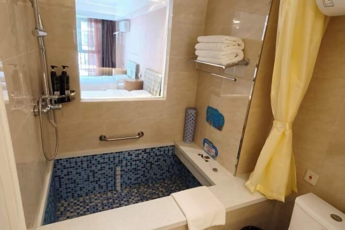 A bathroom with a blue-tiled bathtub, a shower, and a toilet.