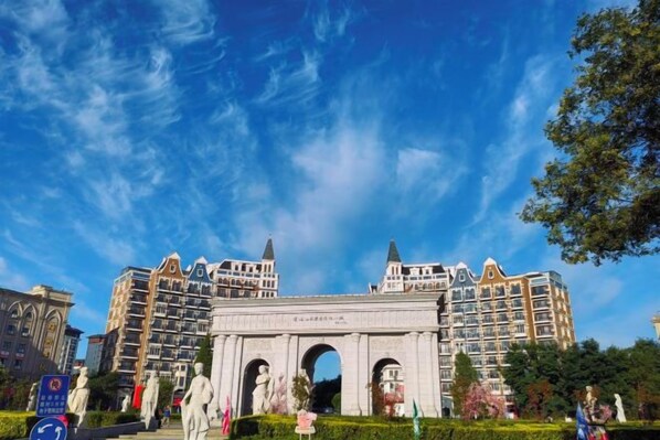 A large, historic archway with multiple arches, surrounded by modern buildings and greenery.