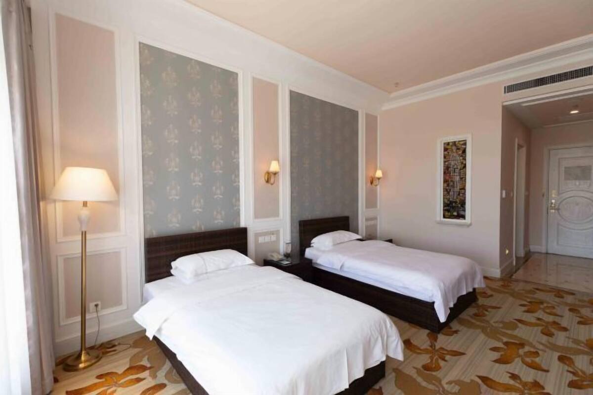 Ein Hotelzimmer mit zwei Einzelbetten, einer Stehlampe und einem gemusterten Teppich.