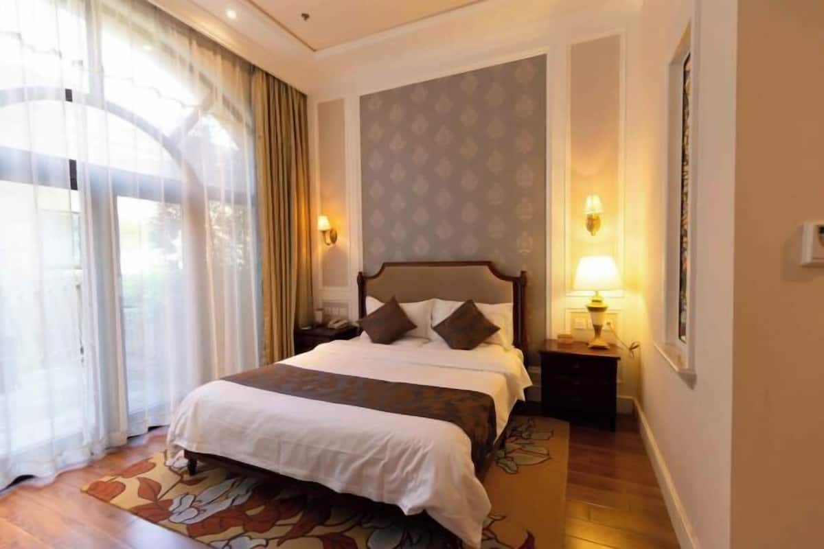 Ein Hotelzimmer mit einem großen Bett, einem Nachttisch, einer Lampe und Blick ins Freie.