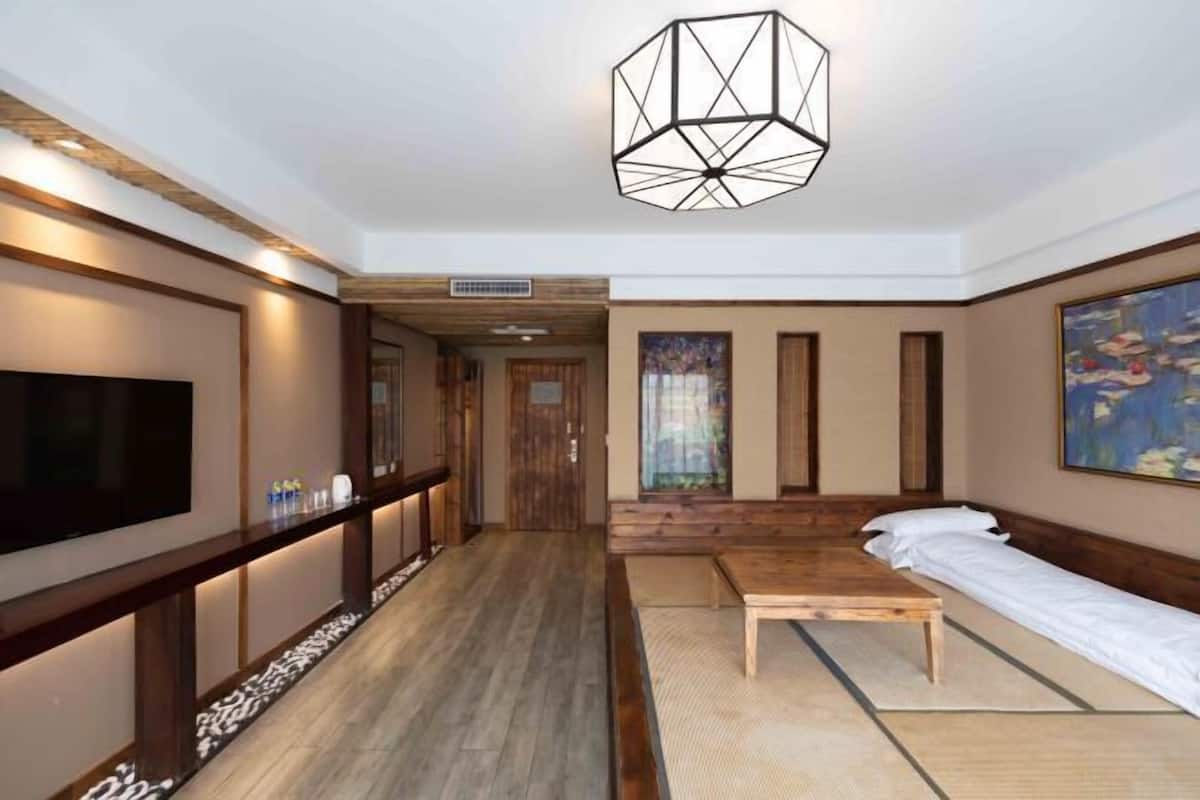 Ein Hotelzimmer mit Holzboden, einem Bett, einem Fernseher, einem Schreibtisch und einem Bild an der Wand.
