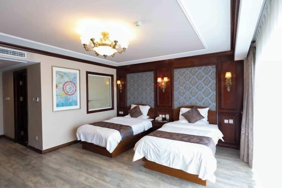 Ein Hotelzimmer mit zwei Betten, einer Kristallleuchtre, Kunstwerken an den Wänden und einem strukturierten Wanddesign.