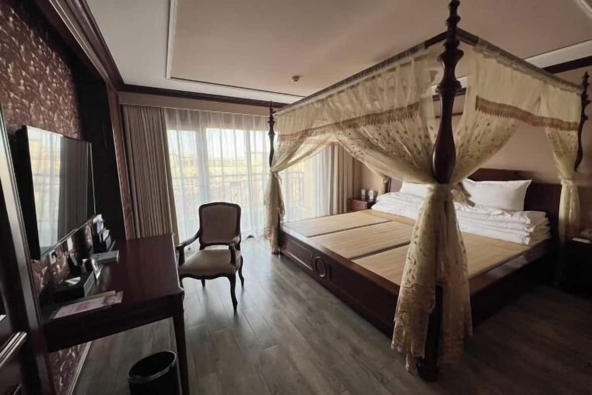 Ein Hotelzimmer mit Himmelbett, Stuhl, Schreibtisch und einem großen Spiegel.