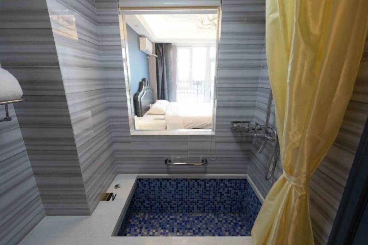 Ein Badezimmer mit Fenster, einer Badewanne mit blauen Mosaikfliesen, einem Handtuchhalter und einer Duschkabine.