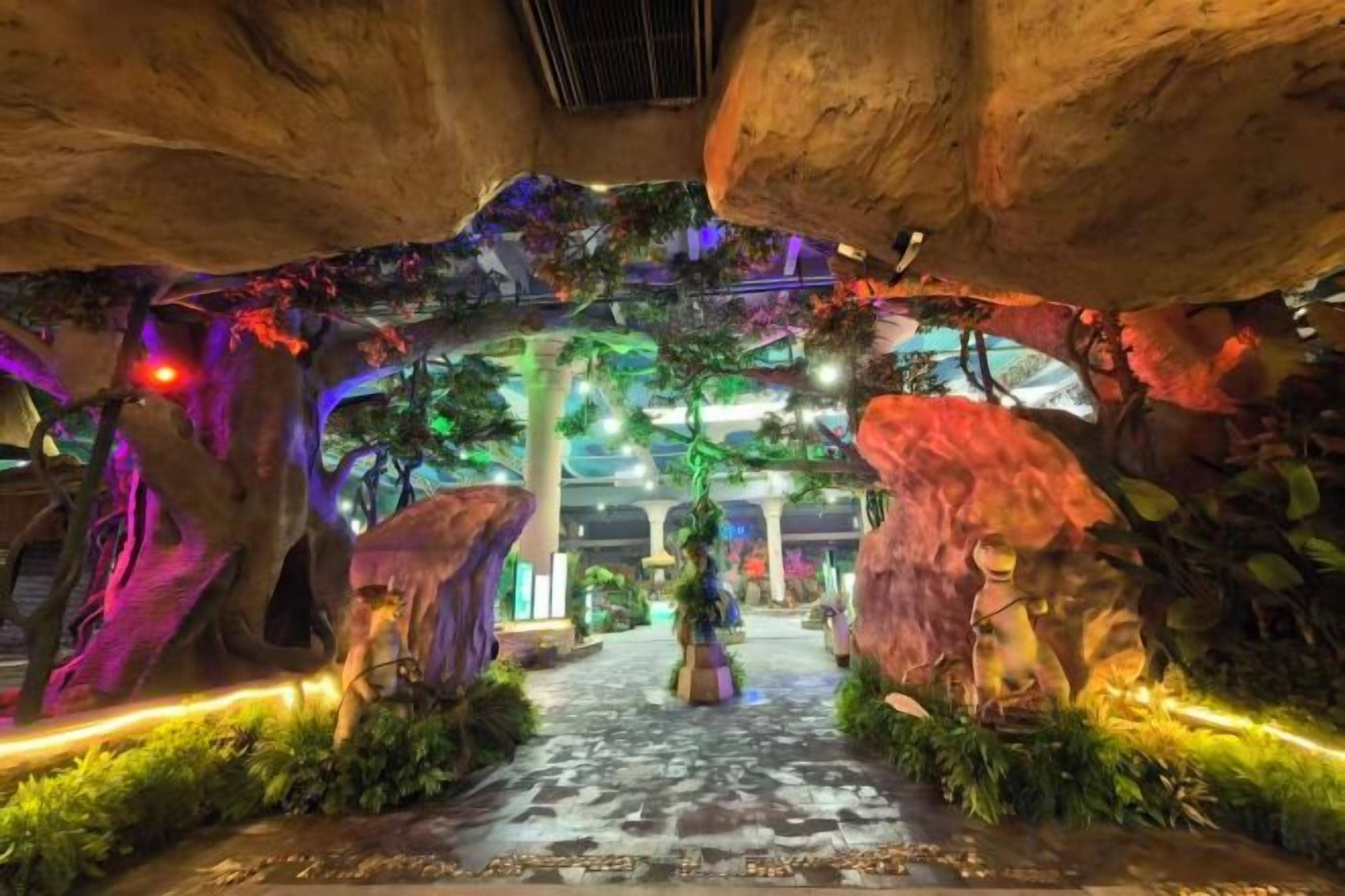 An indoor pathway with artificial rock formations and greenery, leading to a central area with columns.