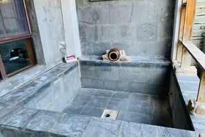 A stone-walled bathroom with a shower area and a window.
