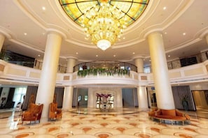 Un'ampia hall con un grande lampadario, colonne e una zona salotto circolare.