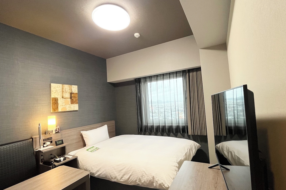 A hotel room with a bed, bedside table, lamp, and a painting on the wall.
