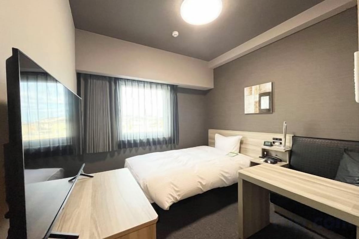 A hotel room with a bed, a desk, a television, and a window with curtains.