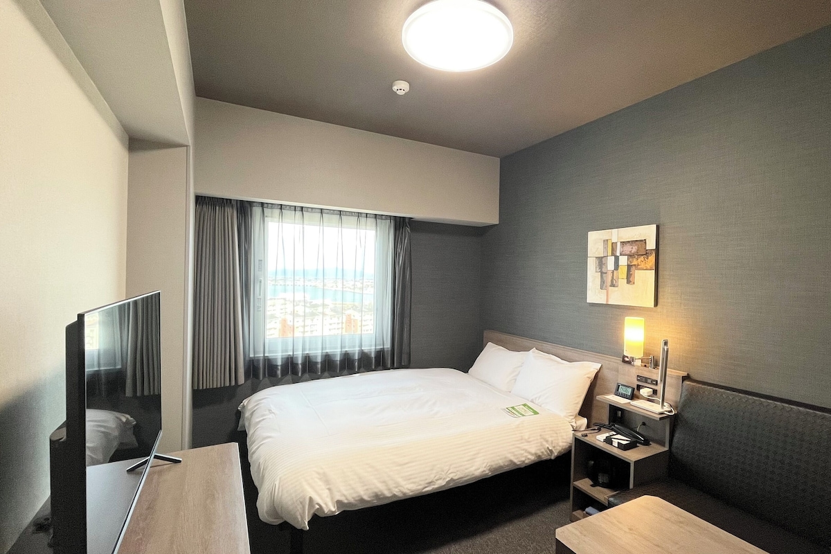A hotel room with a bed, bedside table, lamp, and a painting on the wall.