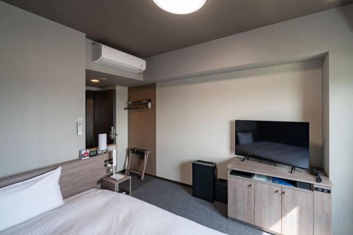 A hotel room with a bed, a television, a desk with a computer, and a wardrobe.