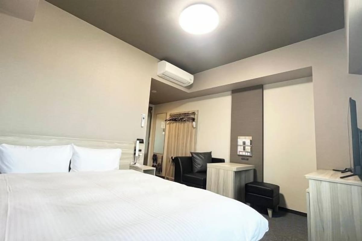 A hotel room with a large bed, a desk, a chair, and a television.