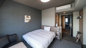 Ein Hotelzimmer mit Bett, Schreibtisch, Stuhl, Nachttisch, Spiegel und einer Tür zu einem anderen Raum.