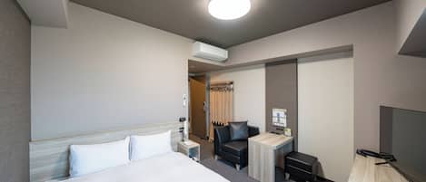 A hotel room with a large bed, a desk, a chair, a TV, and an air conditioning unit.