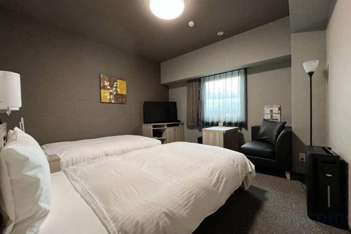 A hotel room with two beds, a television, a desk, a chair, and a lamp.