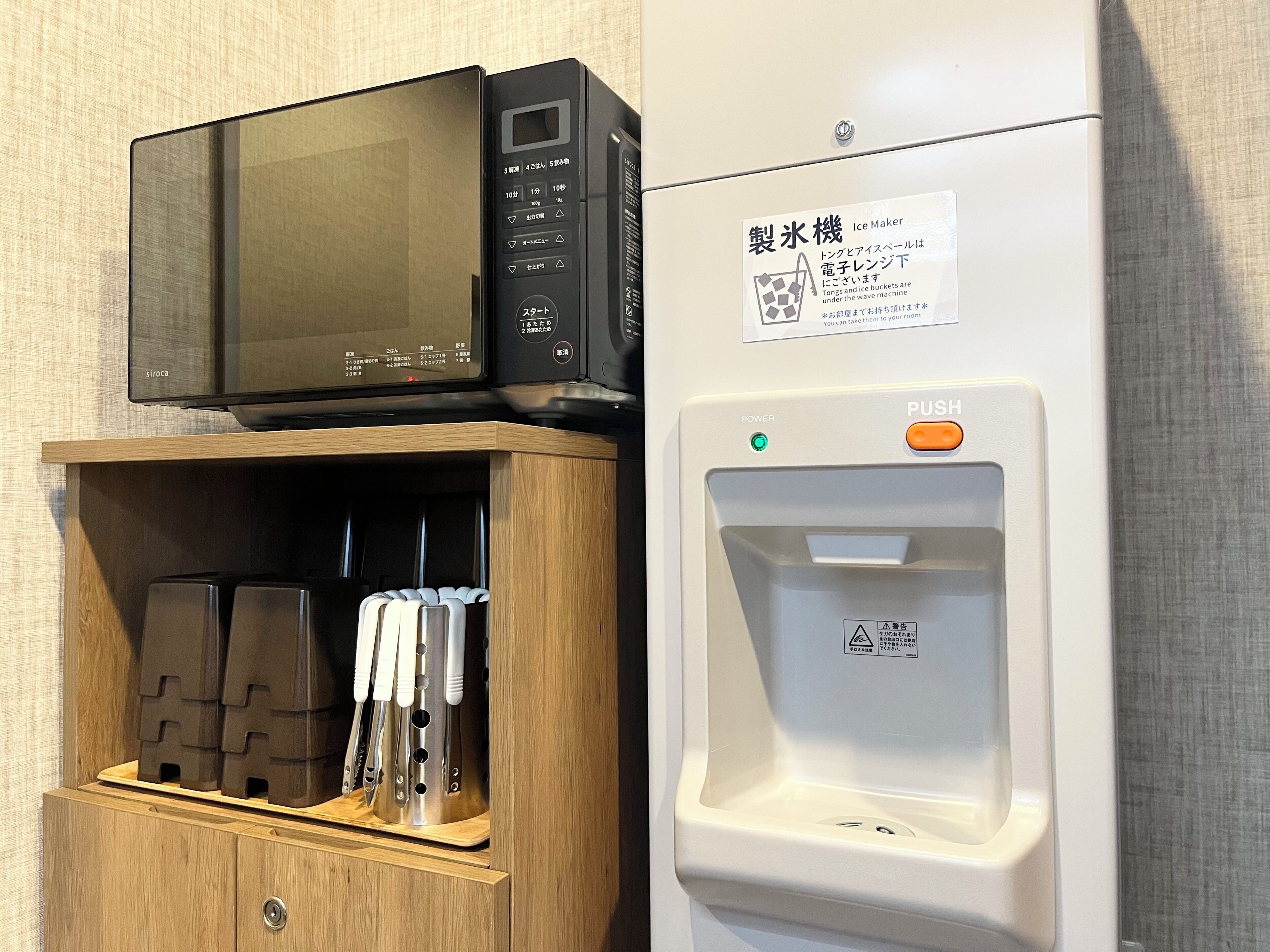 A microwave on a shelf, a water dispenser, and a cabinet with utensils.