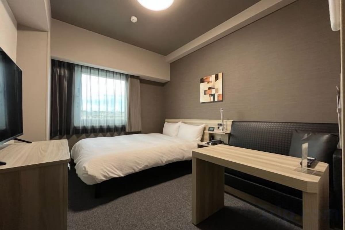 A hotel room with a bed, bedside table, and a desk with a chair.