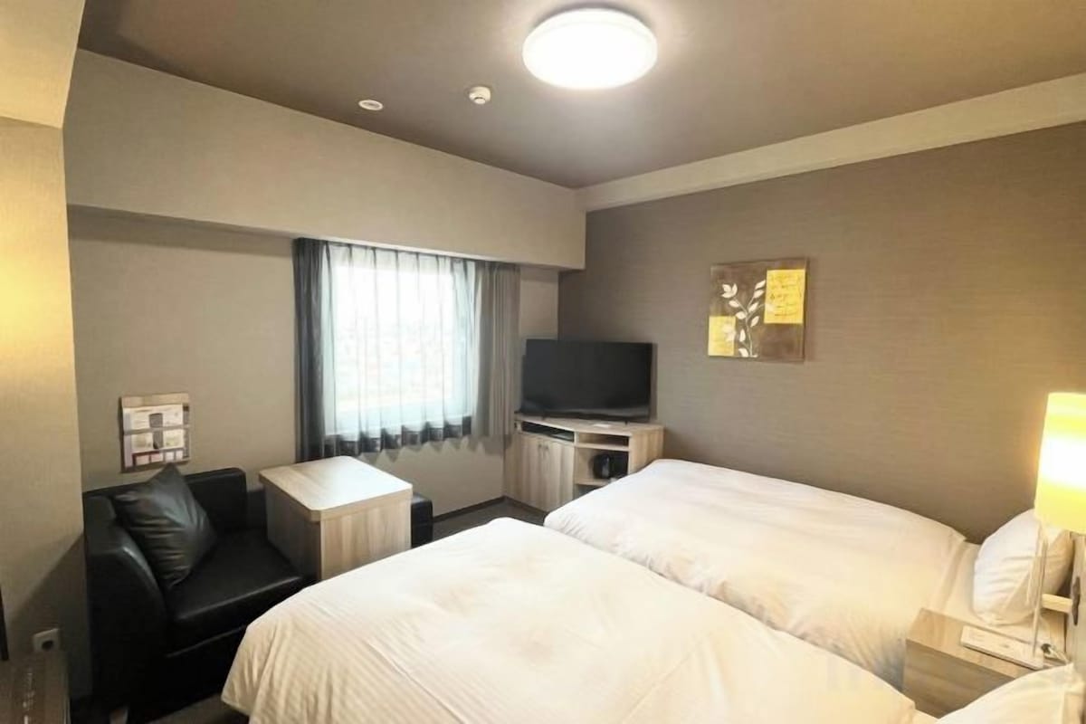 A hotel room with two beds, a TV, a desk, and a sofa.