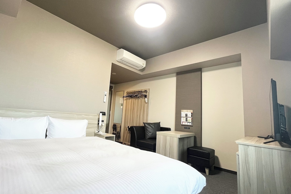 A hotel room with a large bed, a desk, a chair, an air conditioning unit, and a television.