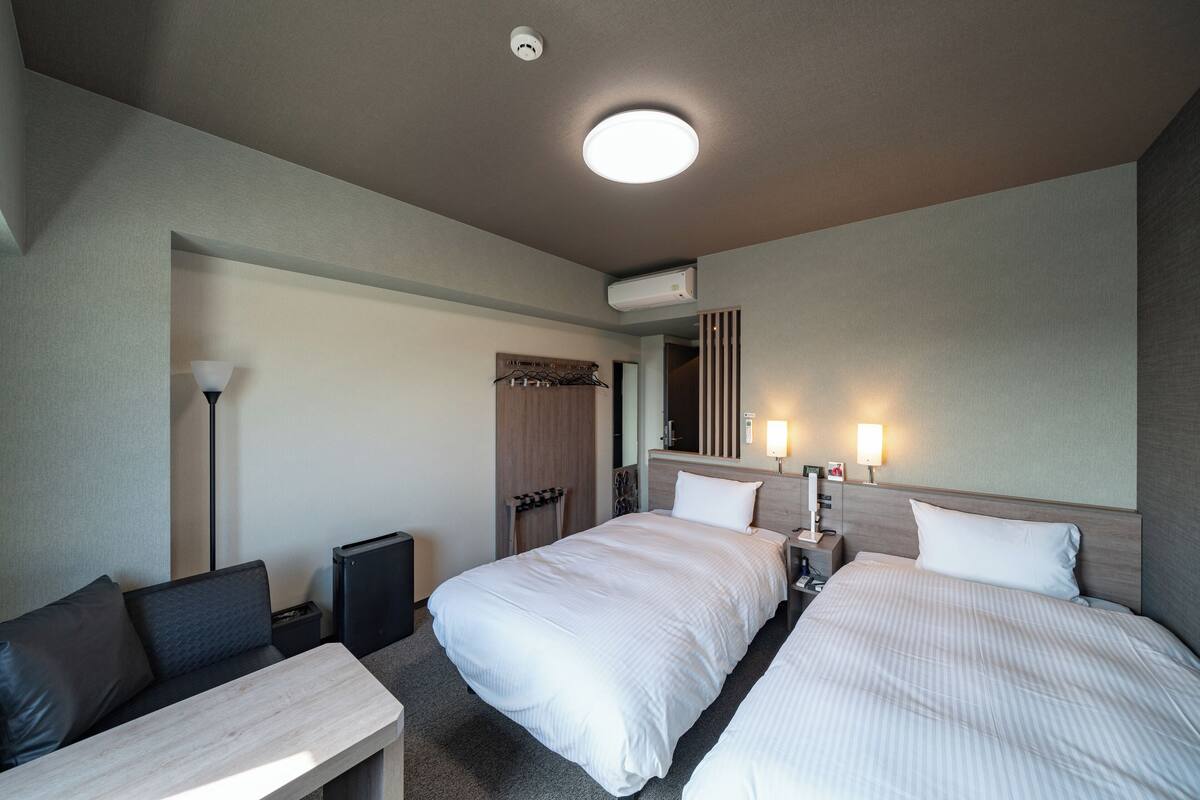 A hotel room with two beds, a desk, a lamp, a wardrobe, and a ceiling light.