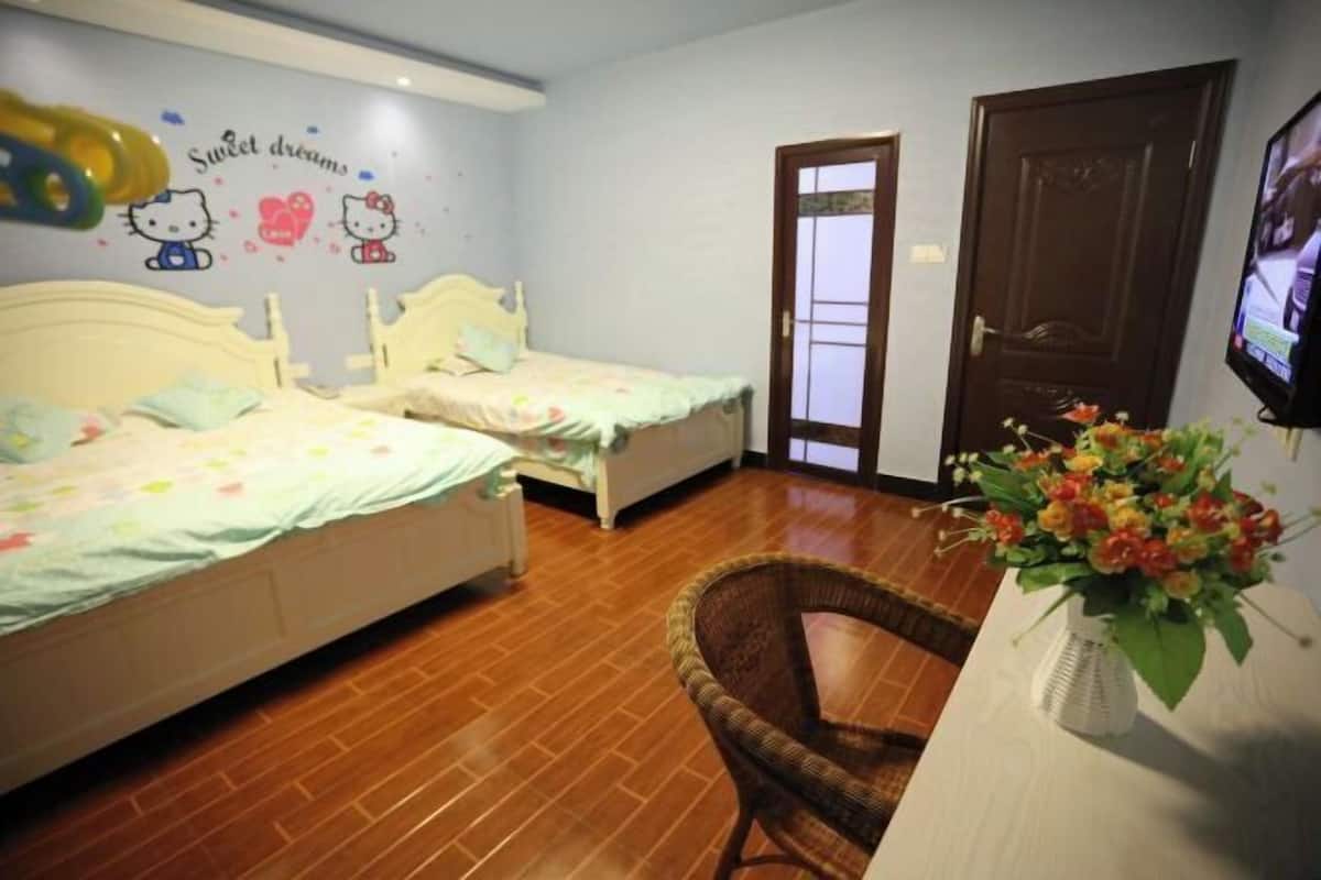 A bedroom with two single beds, a wicker chair, a TV, and a wall with Hello Kitty decorations.